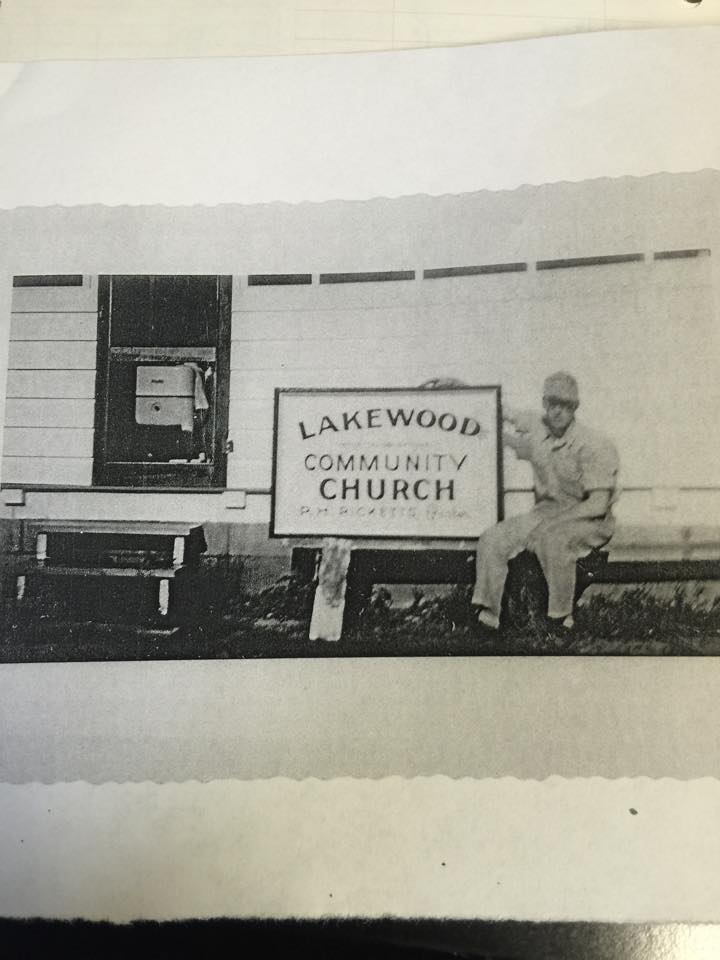 Pastor R. H. Ricketts seated beside the Lakewood Community Church sign